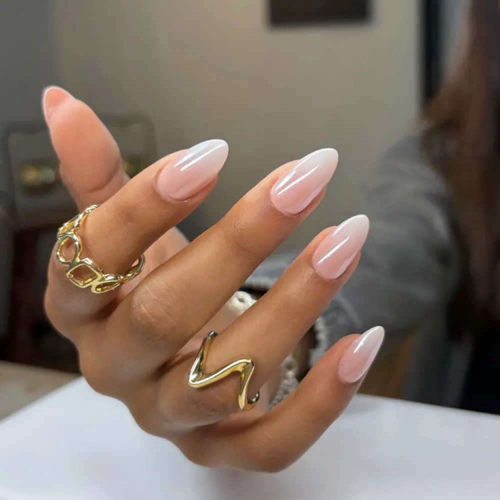 A milky almond-shaped Gel-X nail extension set with gold rings